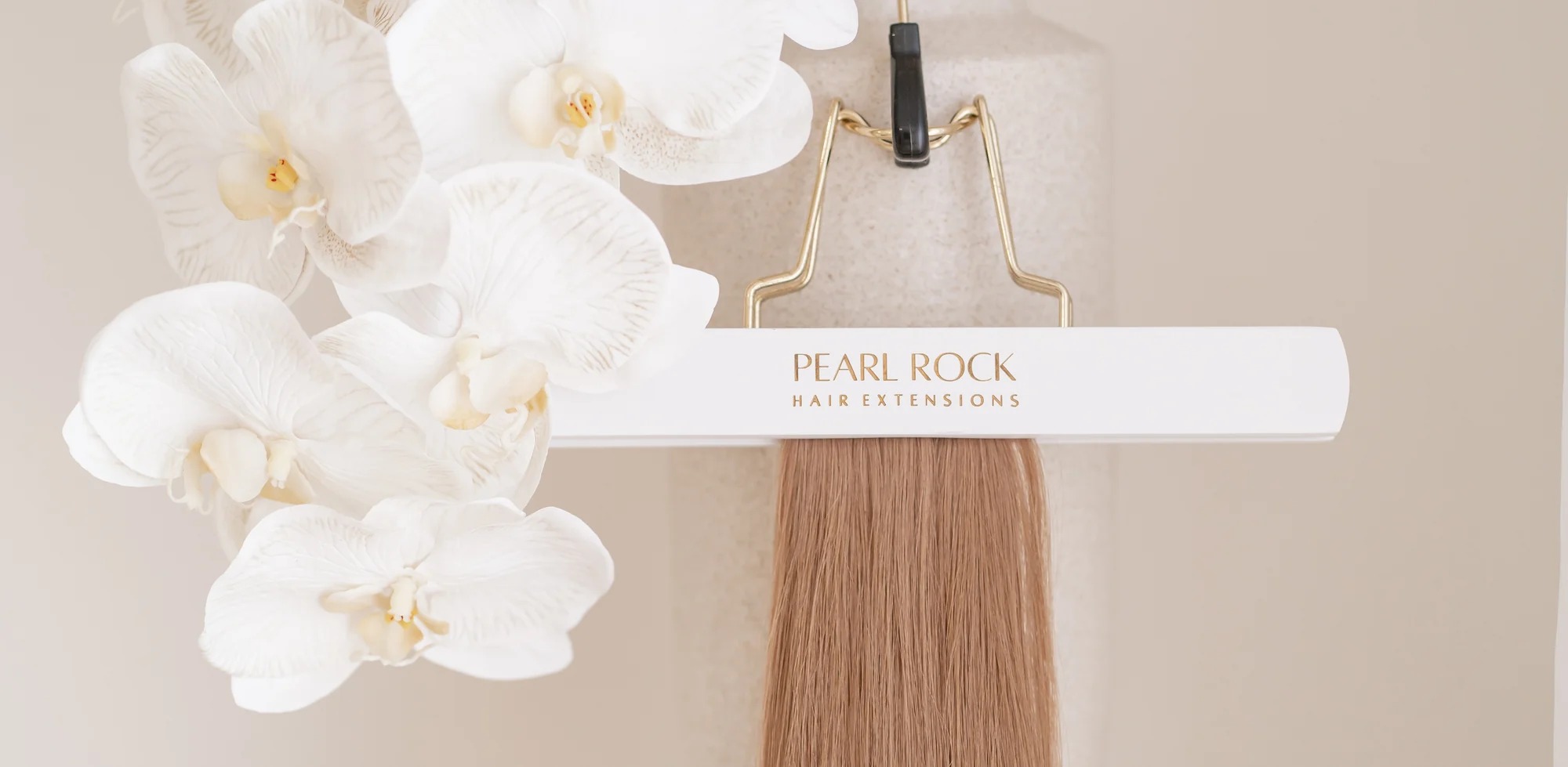 Pearl Rock Hair Extensions weft on a branded hanger beside white orchids